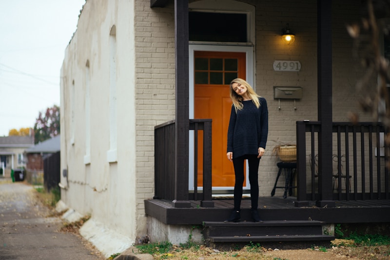 A young woman steps onto the porch of a small house in morning light, holding a coffee cup.